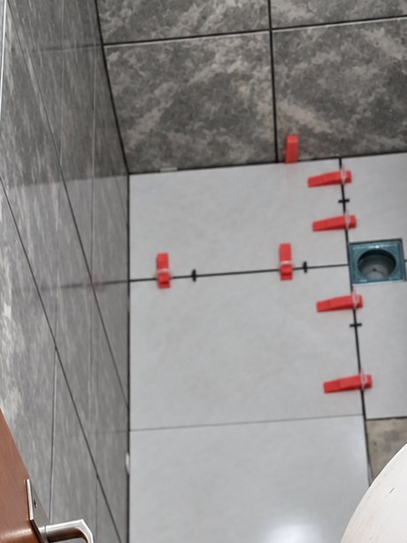Box de banheiro sendo revestido em porcelanato marmorizado cinza, com espaçadores niveladores e ralo