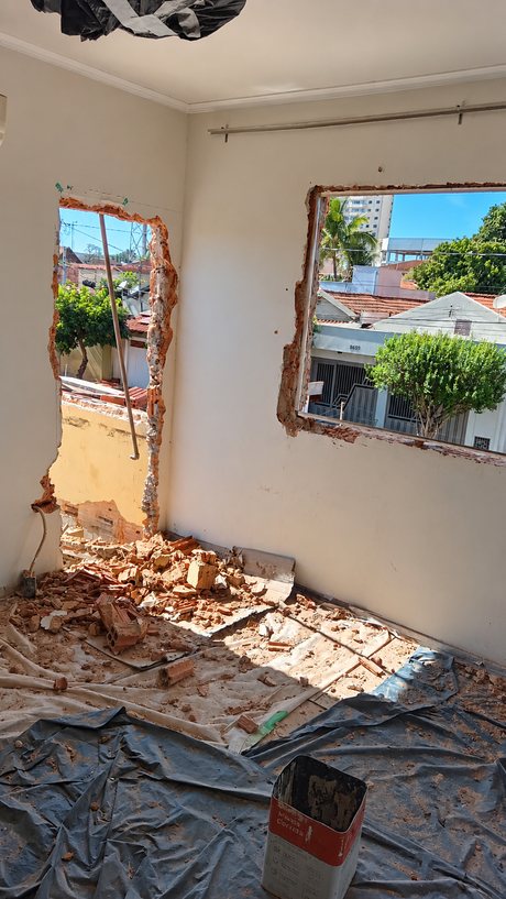 Quarto com dois vãos de janela abertos na alvenaria e o piso protegido com lona